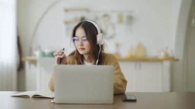 Gözlüklü ve kulaklık takan Asyalı genç bir kadın evde bilgisayar bilgisayarı üzerinde çalışıyor. Evde çalışmak, video konferansı, video çağrısı, öğrenci öğrenme çevrimiçi sınıf