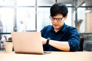 Asyalı işadamı gözlük takıyor ve ofiste çalışıyor. İş yerindeki bilgisayarda çalışan yakışıklı genç adam.