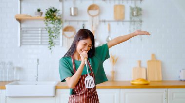 Asyalı genç bir kadın mutfak odasında dans ediyor. Hafta sonları boş zamanlarında mutlu ve rahatlatıcı bir kadın.