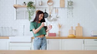 Asyalı genç bir kadın mutfak odasında dans ediyor. Hafta sonları boş zamanlarında mutlu ve rahatlatıcı bir kadın.