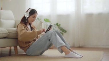 Mutlu Asyalı kadın evde dinleniyor. Kanepede oturan ve elinde cep telefonu tutan bir kadın gülümsemesi. Kız arkadaşa video çağrısı yapıyor