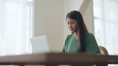 Evde çalışan genç Asyalı kadın. Evdeki masada bilgisayar kullanan bir kadın.