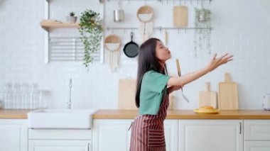Asyalı genç bir kadın mutfak odasında dans ediyor. Hafta sonları boş zamanlarında mutlu ve rahatlatıcı bir kadın.