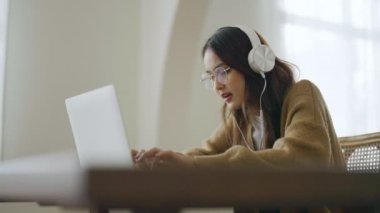 Gözlüklü ve kulaklık takan Asyalı genç bir kadın evde bilgisayar bilgisayarı üzerinde çalışıyor. Evde çalışmak, video konferansı, video çağrısı, öğrenci öğrenme çevrimiçi sınıf