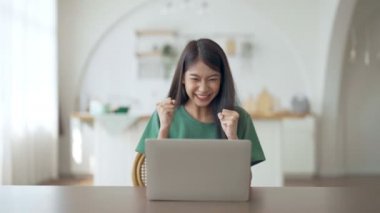 Asyalı bir kadının kazanmasını ya da bilgisayar laptopunda ecommerce alışveriş teklifi almasını kutlayan komik bir coşku. Heyecanlı mutlu kız kazanan başarıyı kutlayan deftere bakıyor.