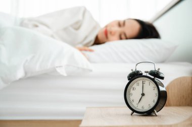 Genç Asyalı kadın sabah yatak odasında mutlu bir uyku çekiyor. Beyaz yatakta çalar saatin kapanışı
