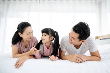 Mutlu Asyalı aile bireyleri yatak odasında birlikte vakit geçiriyorlar. Anne ve baba ve kızı yatakta dinleniyorlar ve eğleniyorlar.