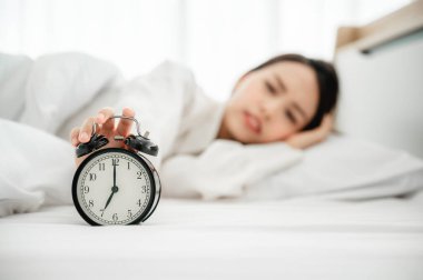 Genç Asyalı kadın sabah erken kalkar. Yatakta uzanıyor ve alarmı kapatmaya çalışıyor.