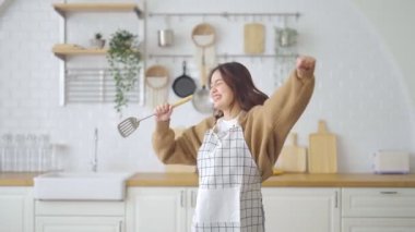 Asyalı genç bir kadın mutfak odasında dans ediyor. Hafta sonları boş zamanlarında mutlu ve dinleniyor.