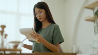 Mutfakta gözlük takan mutlu genç Asyalı kadın. Kadın yoğunlaştırılmış okuma notu pişirme