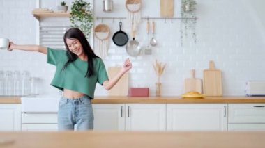 Asyalı genç bir kadın mutfak odasında dans ediyor. Hafta sonları boş zamanlarında mutlu ve rahatlatıcı bir kadın.