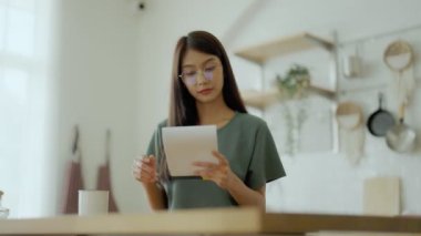 Mutfakta gözlük takan mutlu genç Asyalı kadın. Kadın yoğunlaştırılmış okuma notu pişirme