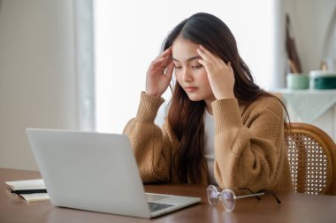 Ofis sendromu. Çok çalışan yorgun Asyalı kadın baş ağrısı çekiyor, bilgisayardan sonra görme sorunu yaşıyor. Stresli genç kadın evde yorgunluk çekiyor.