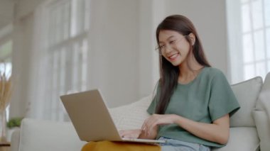 Evde dizüstü bilgisayarla çalışan gülümseyen Asyalı kadın. Çekici Asyalı kadın bilgisayar eğitimi kullanıyor, çevrimiçi eğitim ve video çağrısı izliyor.