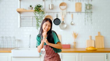 Asyalı genç bir kadın mutfak odasında dans ediyor. Hafta sonları boş zamanlarında mutlu ve rahatlatıcı bir kadın.