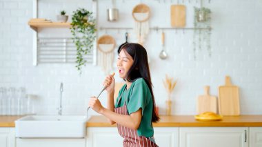 Asyalı genç bir kadın mutfak odasında dans ediyor. Hafta sonları boş zamanlarında mutlu ve rahatlatıcı bir kadın.
