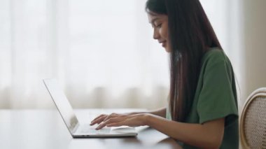 Ev bilgisayarında çalışan gülümseyen Asyalı genç kadın. Genç Asyalı öğrenci bilgisayar eğitimi alıyor, sanal eğitim alıyor, e-öğreniyor, evde online eğitim webinar izliyor.