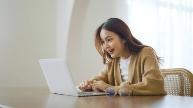 Ev bilgisayarında çalışan gülümseyen Asyalı genç kadın. Genç Asyalı öğrenci bilgisayar eğitimi alıyor, sanal eğitim alıyor, e-öğreniyor, evde online eğitim webinar izliyor.