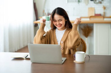 Asyalı bir kadının kazanmasını ya da bilgisayar laptopunda ecommerce alışveriş teklifi almasını kutlayan komik bir coşku. Heyecanlı mutlu kız kazanan başarıyı kutlayan deftere bakıyor.