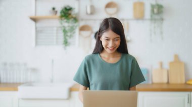 Ev bilgisayarında çalışan gülümseyen Asyalı genç kadın. Genç Asyalı öğrenci bilgisayar eğitimi alıyor, sanal eğitim alıyor, e-öğreniyor, evde online eğitim webinar izliyor.