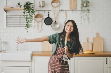 Asyalı genç bir kadın mutfak odasında dans ediyor. Hafta sonları boş zamanlarında mutlu ve dinleniyor.