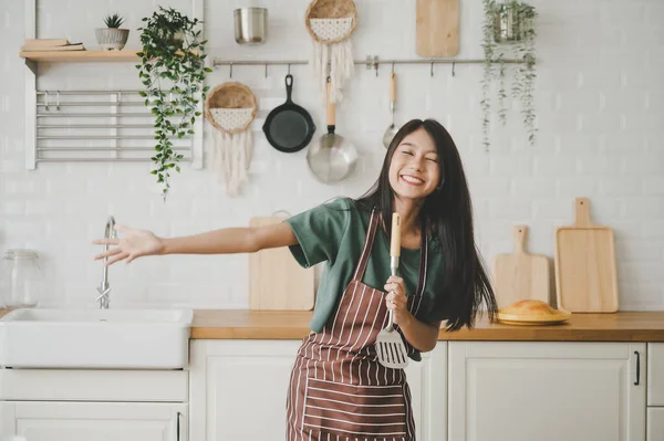 Asyalı genç bir kadın mutfak odasında dans ediyor. Hafta sonları boş zamanlarında mutlu ve dinleniyor.