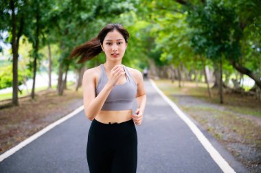 Asian woman running outdoor in public park. Female jogging on the road in morning. Healthy lifestyle concept, sports outdoor activities in park