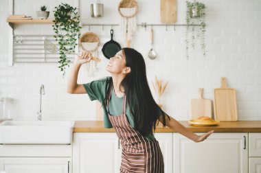 Asyalı genç bir kadın mutfak odasında dans ediyor. Hafta sonları boş zamanlarında mutlu ve dinleniyor.