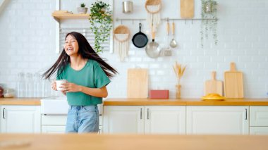 Asyalı genç bir kadın mutfak odasında dans ediyor. Hafta sonları boş zamanlarında mutlu ve rahatlatıcı bir kadın.
