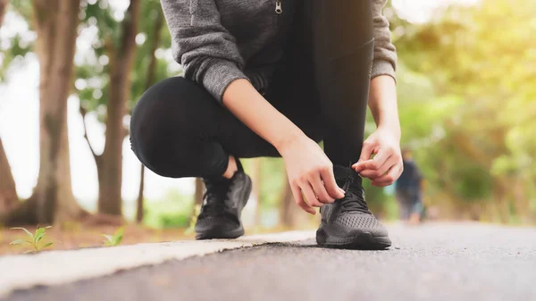 Closeup of woman tying shoe laces. Asian female sport fitness runner getting ready for jogging outdoors in public park