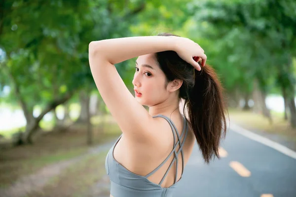 Asian woman trainer is engaged in fitness in public park. Sporty woman does exercises in the open air. Healthy lifestyle, sports outdoor activities in park