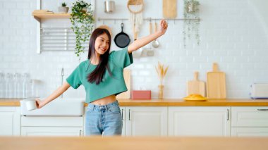 Asyalı genç bir kadın mutfak odasında dans ediyor. Hafta sonları boş zamanlarında mutlu ve rahatlatıcı bir kadın.