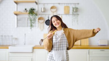 Asyalı genç bir kadın mutfak odasında dans ediyor. Hafta sonları boş zamanlarında mutlu ve dinleniyor.