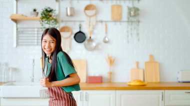 Asyalı genç bir kadın mutfak odasında dans ediyor. Hafta sonları boş zamanlarında mutlu ve rahatlatıcı bir kadın.