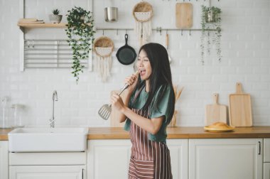 Asyalı genç bir kadın mutfak odasında dans ediyor. Hafta sonları boş zamanlarında mutlu ve dinleniyor.