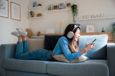 Mutlu Asyalı kadın evde dinleniyor. Kanepede oturan ve elinde cep telefonu tutan bir kadın gülümsemesi. Arkadaşı ile görüntülü konuşma yapan bir kız. Müzik dinliyordum.