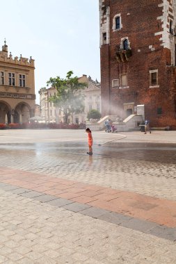 KRAKOW, POLAND - 26 Haziran 2016: Güneşli bir yaz gününde ana Pazar Meydanı 'nda su perdesi kullanan küçük bir kız. Şehrin çeşitli yerlerindeki büyük sıcaklıklarda itfaiyeciler perdeleri yerleştiriyor.