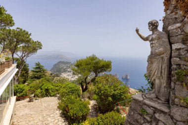 Capri Adası; İtalya - 28 Haziran 2021: Monte Solaro adasının tepesinden Tyrhenian Denizi 'ne Faraglioni kayaları ile hava manzarası; İmparator Augustus' un önplandaki heykeli
