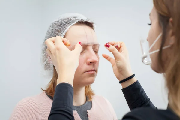 Kaş dövmesi. Usta bir iplik kullanarak gelecekteki kaşlarını çiziyor.