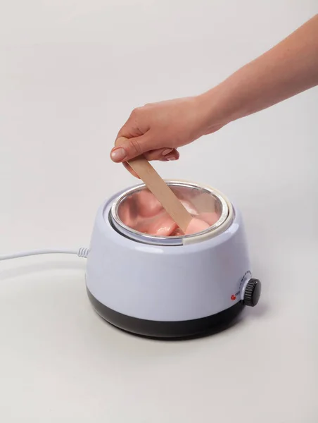 Beyaz arka planda balmumu eriticisi. Salon ekipmanları. Ahşap spatula kadın ellerinde..