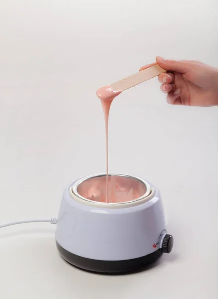 Wax melter on a white background. Salon equipment. Wooden spatula in female hands.