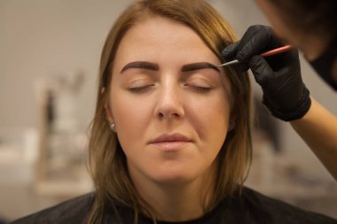 Güzel genç bir kadın kaş düzeltme prosedürünü uyguluyor. Güzellik salonunda kaşlarını boyayan genç bir kadın..