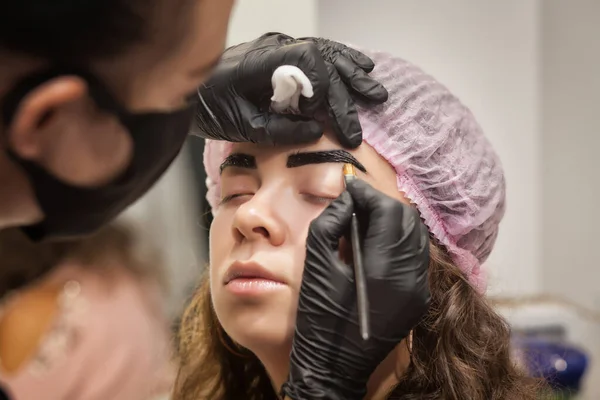 Güzel genç bir kadın kaş düzeltme prosedürünü uyguluyor. Güzellik salonunda kaşlarını boyayan genç bir kadın..