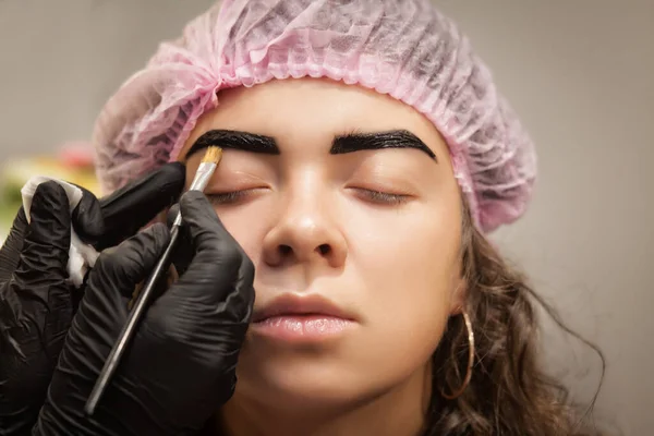 Beautiful young woman gets eyebrow correction procedure.Young woman painting with brush her eyebrows in beauty salon.