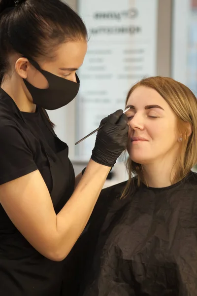 Güzel genç bir kadın kaş düzeltme prosedürünü uyguluyor. Güzellik salonunda kaşlarını boyayan genç bir kadın..