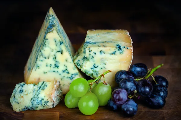 Stilton volwassen blauwe beschimmelde kaas - donkere achtergrond en druiven — Stockfoto