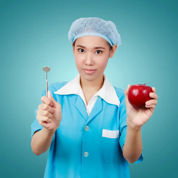 Female dentist holding an apple and metal medical equipment too — Stock Photo, Image