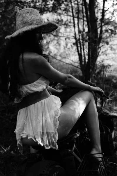 年轻性感的女人 留着长长的波浪般的头发 穿着夏装 头戴草帽 站在摩托车旁边 黑白照片 — 图库照片