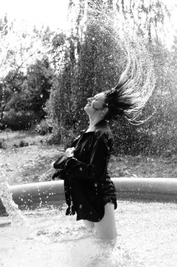 Yüzme havuzunda siyah beyaz pozlar veren koyu renk gömlekli güzel, ıslak bir kadın. 