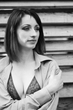 Koyu renk iç çamaşırlı güzel esmer kadın, tahta evin yanındaki deri koltukta poz veriyor. 